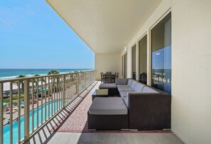 A balcony with a view of the ocean, a seating area with a sofa and chairs, and a pool.