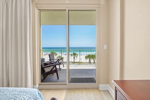 A room with a bed, a desk, and a view of the beach through a sliding door.