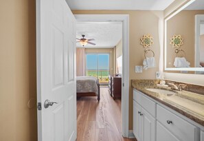 A hotel room with a bed, a bathroom with a sink and mirror, a ceiling fan, and a view of the outside.