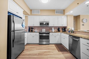 A modern kitchen with white cabinets, stainless steel appliances, and a wooden floor.