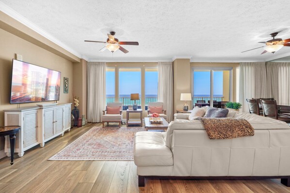 A spacious living room with a large sofa, a television, and a view of the ocean.
