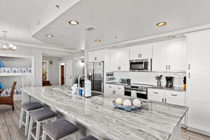 A modern kitchen with white cabinetry, a marble island, and stainless steel appliances.