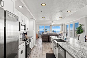 Una cocina moderna con armarios blancos, electrodomésticos de acero inoxidable, encimera de mármol y vistas al océano.