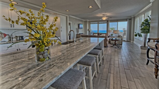 A spacious kitchen with a marble countertop, a built-in island with bar stools, and a view of the ocean through large windows. - 3BR Gulf-Front Retreat | Steps to the Sand (Panama City Beach)