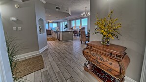 A spacious kitchen with a central island, a dining area with wicker chairs, and a wooden dresser with a vase of yellow flowers. - 3BR Gulf-Front Retreat | Steps to the Sand (Panama City Beach)