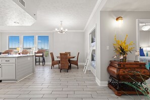 Una cocina amplia con comedor, que cuenta con una isla central, sillas de mimbre y un jarrón decorativo con flores amarillas.