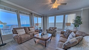 A spacious living room with a large window overlooking a balcony, furnished with leather sofas and a glass coffee table. - 3BR Gulf-Front Retreat | Steps to the Sand (Panama City Beach)