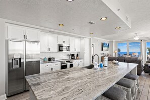 A modern kitchen with white cabinetry, stainless steel appliances, and a marble countertop.