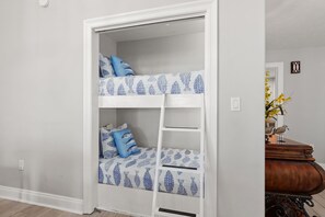 Cama litera con escalera, cómoda y espejo en una habitación con paredes de colores claros.