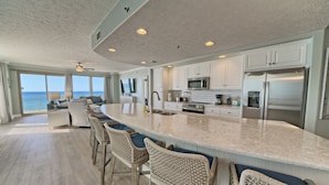 A spacious kitchen with a large island, white cabinetry, stainless steel appliances, and a view to the ocean. - Gulf Crest 301 – 3BR Haven with 360° Views of PCB! (Panama City Beach)