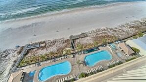 Vista aérea de un complejo turístico en la playa con dos piscinas, una playa y un paseo marítimo que conduce a la misma.