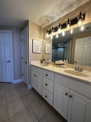 A bathroom with a double sink vanity, a large mirror, and a light fixture above the mirror. - Gulf Crest 1504 | Your Perfect PCB Beachfront Getaway! (Panama City Beach)