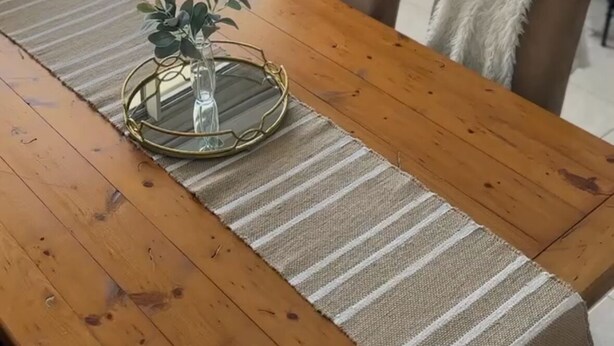 Una mesa de madera para comer con un mantel a rayas y una bandeja de vidrio con una planta.