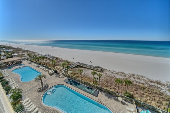 A resort with two swimming pools, a beach, and a clear view of the ocean.