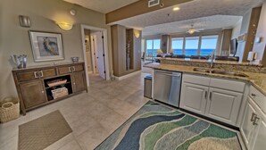 A spacious kitchen with granite countertops, white cabinets, and a view to the outside. - Gulf Crest 606: Escape to a Cozy 2-Bedroom with Gulf Views! (Panama City Beach)