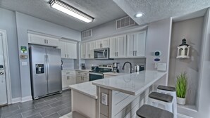 Cocina moderna con armarios blancos, electrodomésticos de acero inoxidable y una isla central con taburetes.