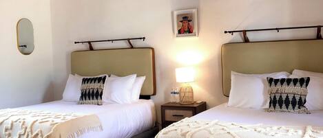 A hotel room with two beds, a wooden ceiling, a patterned floor, and a small bedside table with a lamp.