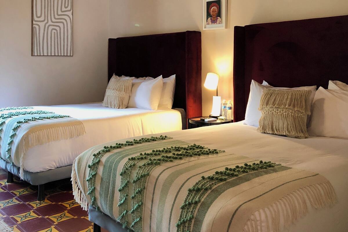 Habitación de hotel con dos camas, una araña, un cuadro enmarcado y una alfombra estampada.