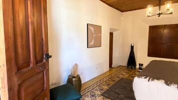Una habitación con techo de madera, una cama con manta gris, un tapete estampado, una puerta de madera y un aplique de pared.