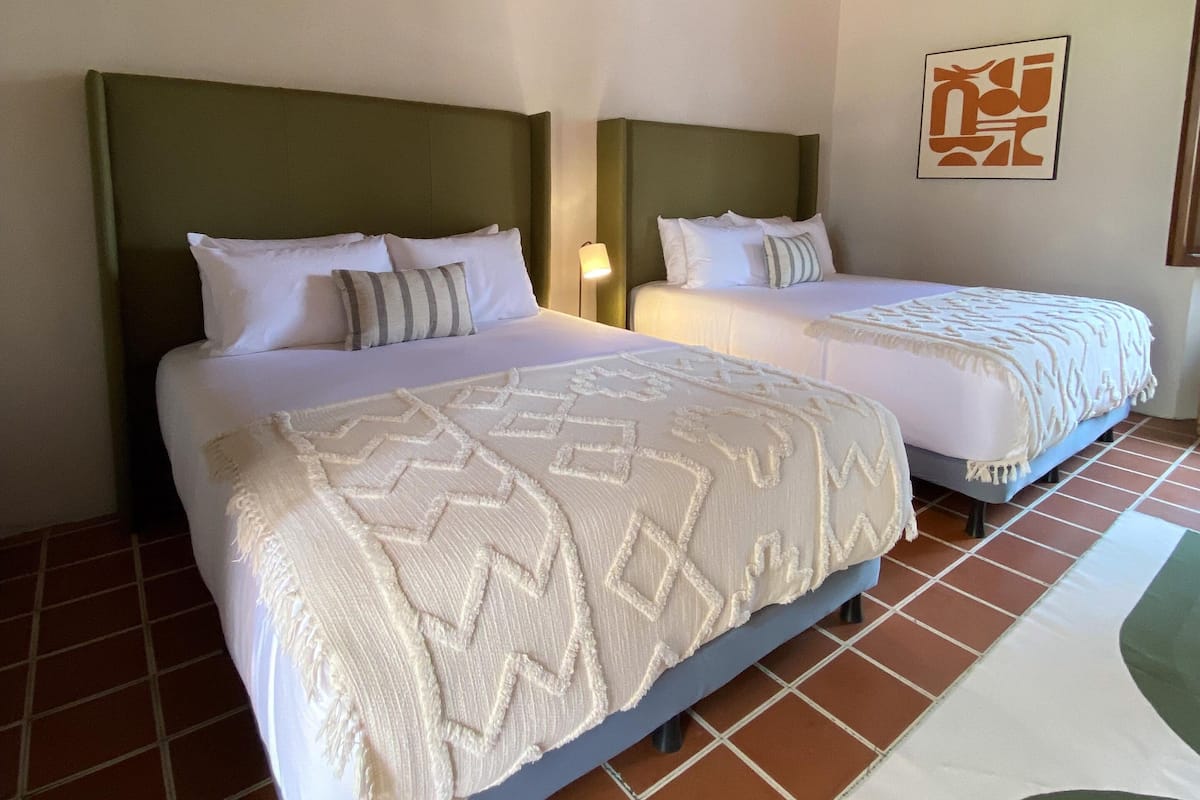 Una habitación de hotel con dos camas, techo de madera y suelo de baldosas.
