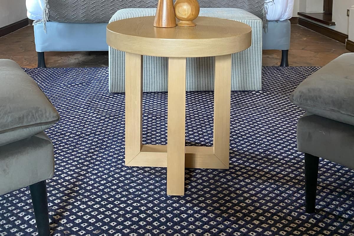 Una habitación con un sofá azul, una mesa redonda de madera con dos jarrones y alfombras estampadas.