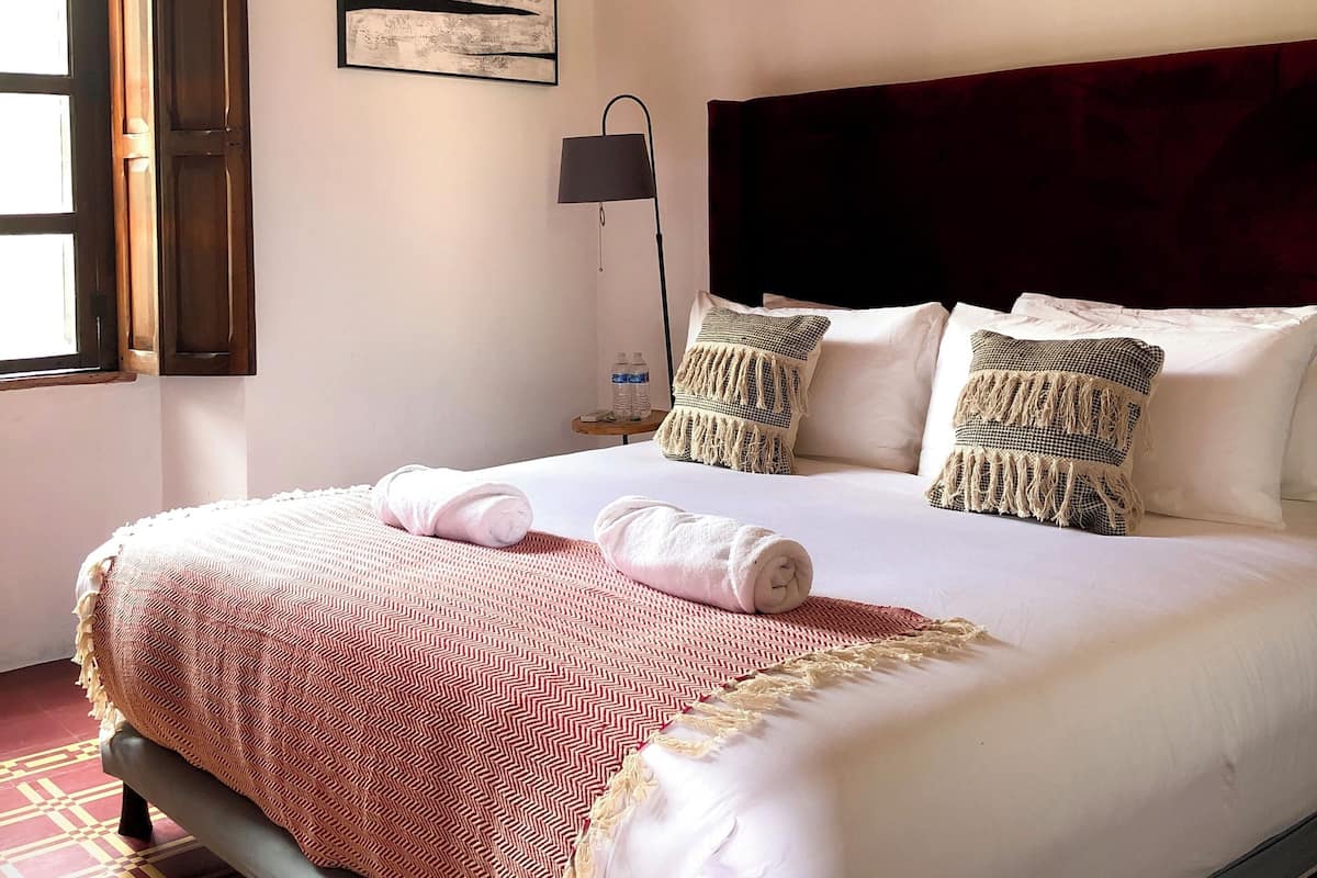 Una cama bien hecha con una colcha estampada, dos almohadas y una lámpara de noche.