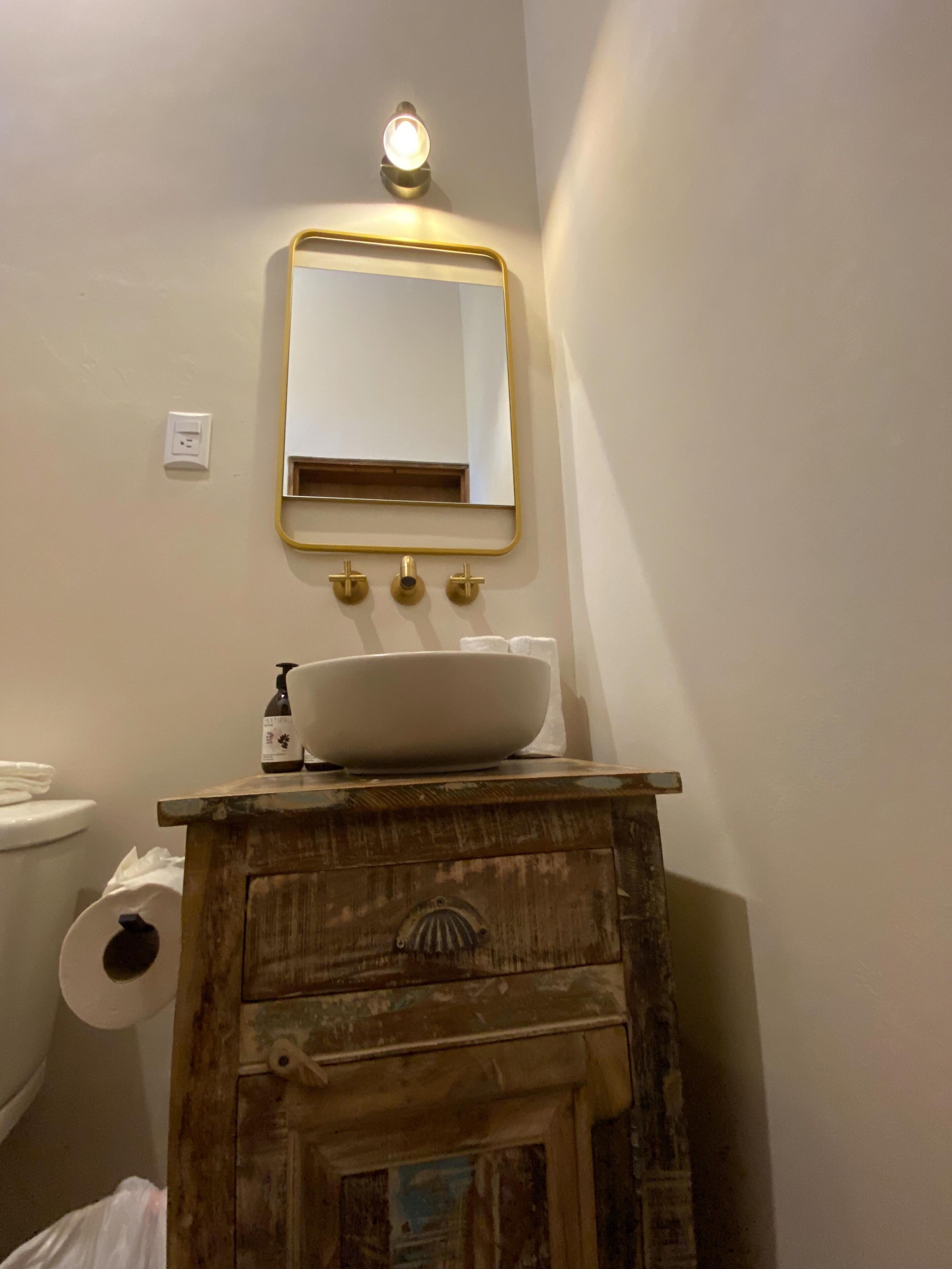Un baño con un lavamanos blanco, un espejo con marco dorado y un mueble de tocador de madera.