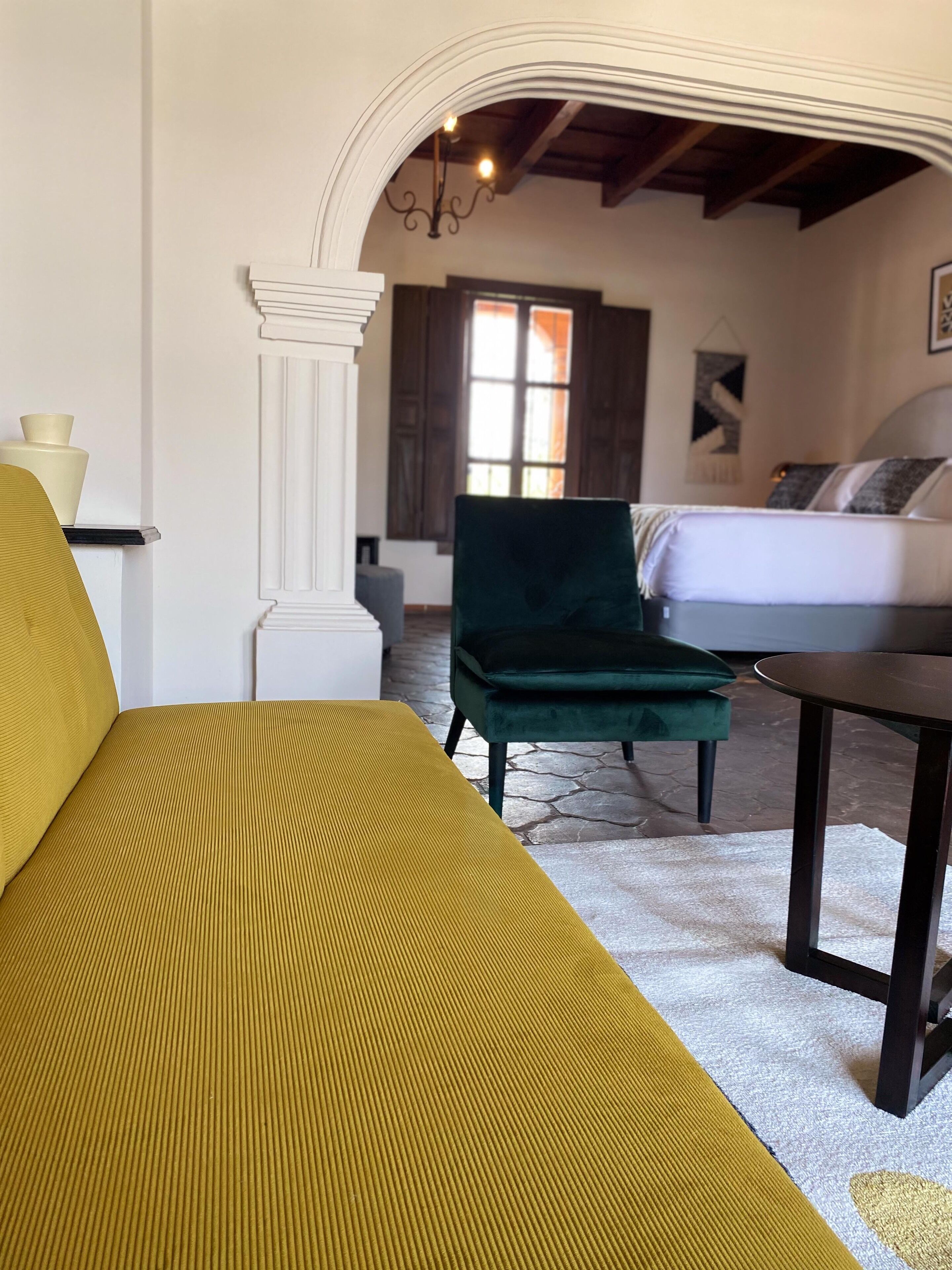 Um quarto com um sofá, uma poltrona verde, uma mesinha e uma cama.