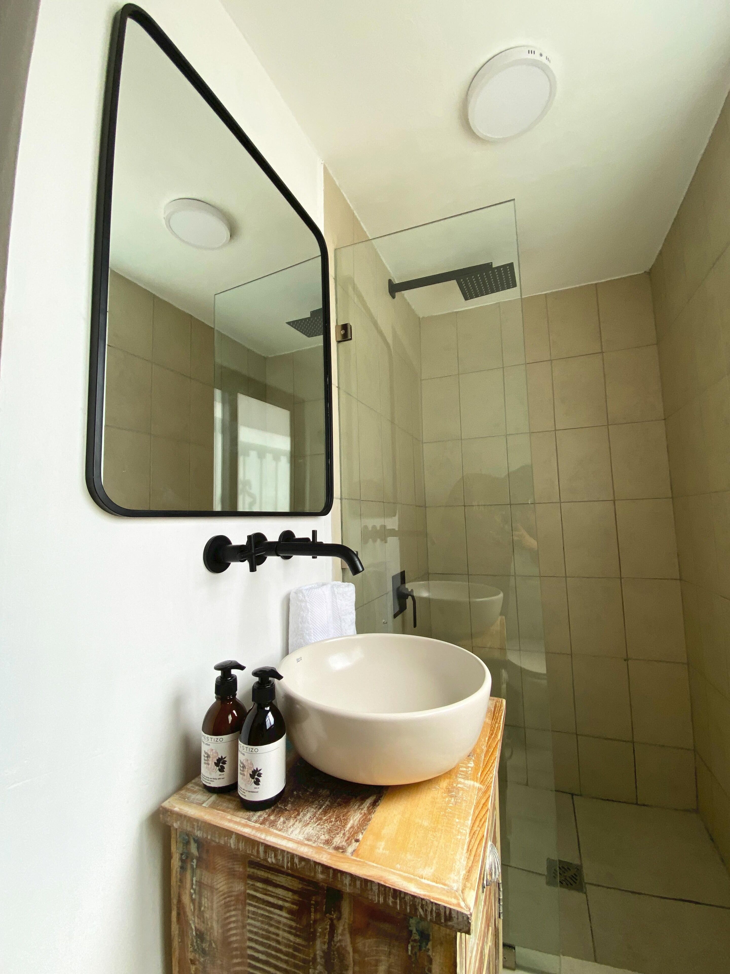 Un baño con lavamanos blanco, espejo y ducha.