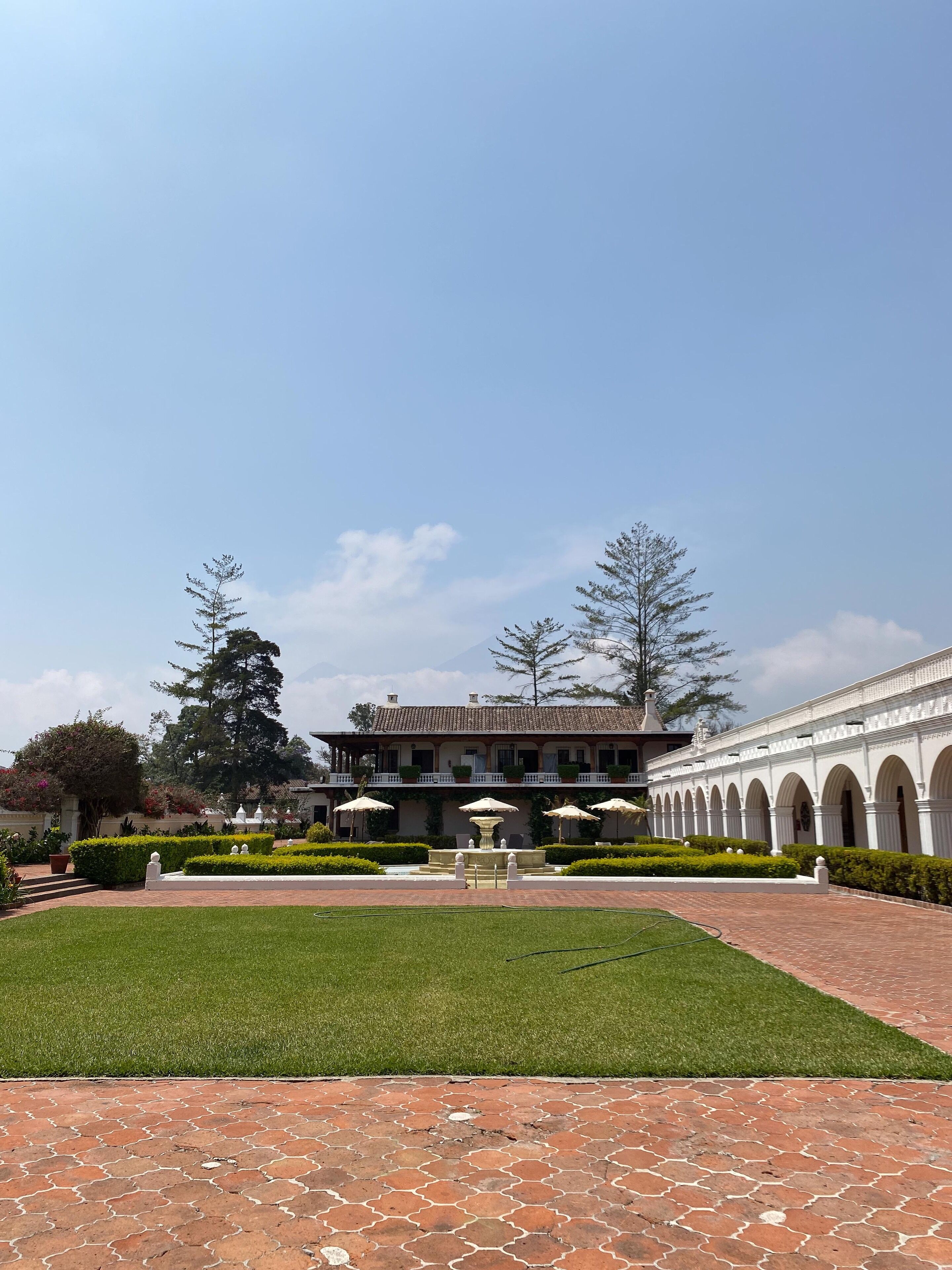 A courtyard with a fountain, a building with a tiled roof, and a white colonnade.