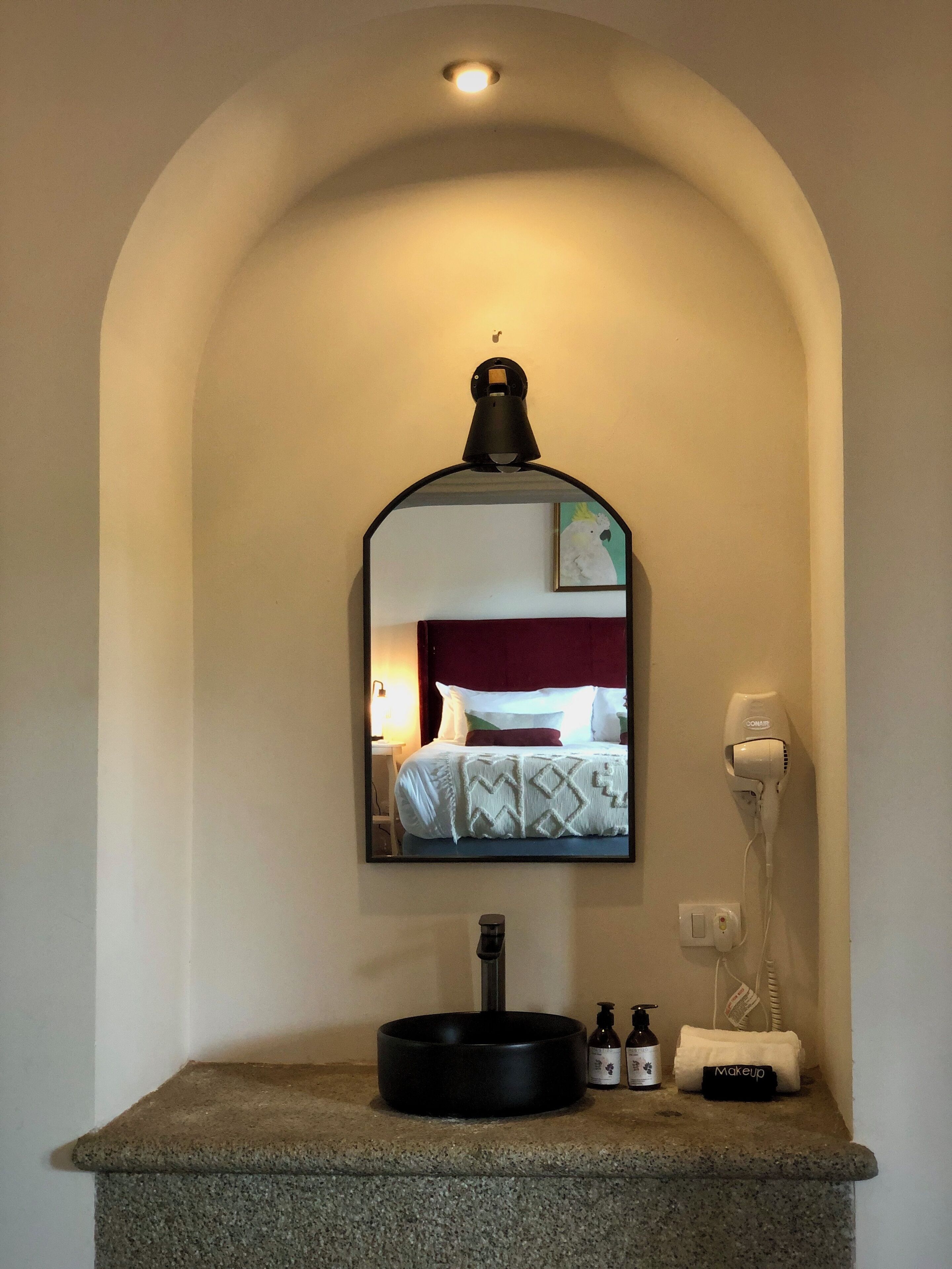 A bathroom with a mirror, a sink, a hairdryer, and toiletries.