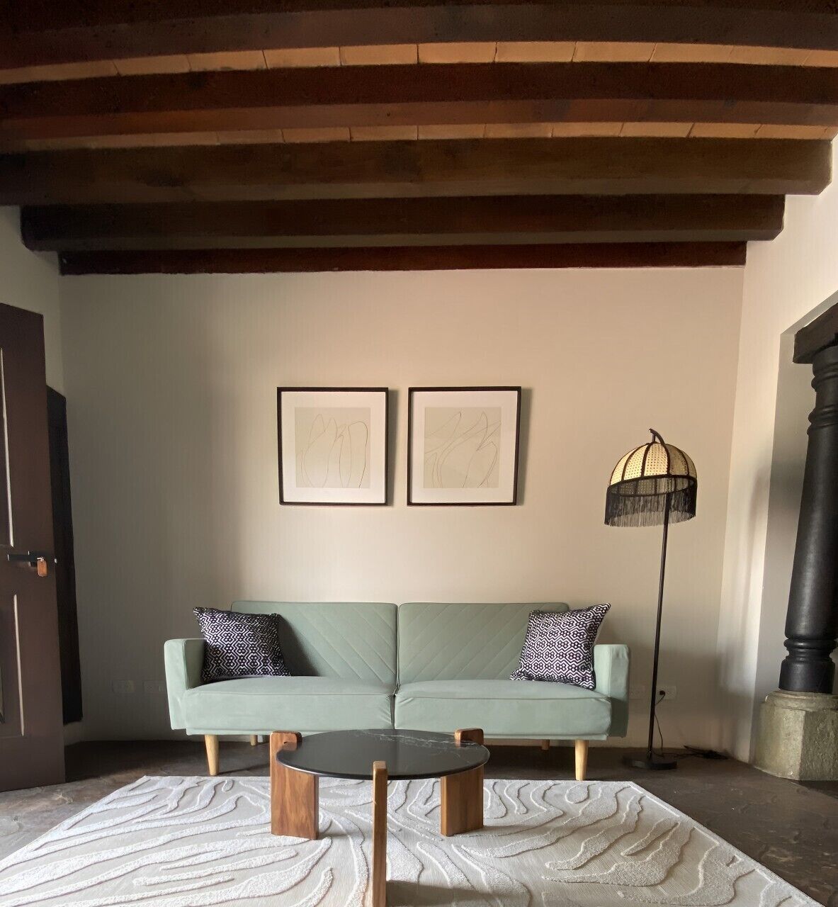 A living room with a light green sofa, two framed abstract artworks, a round coffee table, a floor lamp, and a patterned rug.