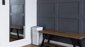 Una habitación con un banco, un espejo grande y un cubo de basura blanco.