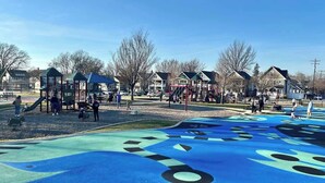 Un parque infantil con suelo azul y negro, rodeado de casas y árboles.
