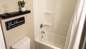A bathroom with a toilet, a shower, and a sink. There is a sign above the toilet that says "Bathroom" and lists services like "Vash," "Brush," "Floss," and "Brush."
