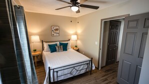 A bedroom with a bed, two bedside lamps, a ceiling fan, and a door.