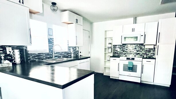 A modern kitchen with white cabinetry, a central island, and a dark floor.