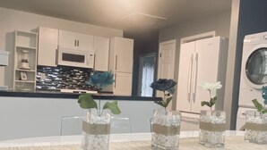 A modern kitchen with white cabinets, a microwave, and a dishwasher. There are four glass vases with plants on the dining table.