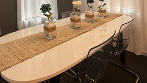 A dining area with a long table, clear chairs, and decorative vases with flowers.
