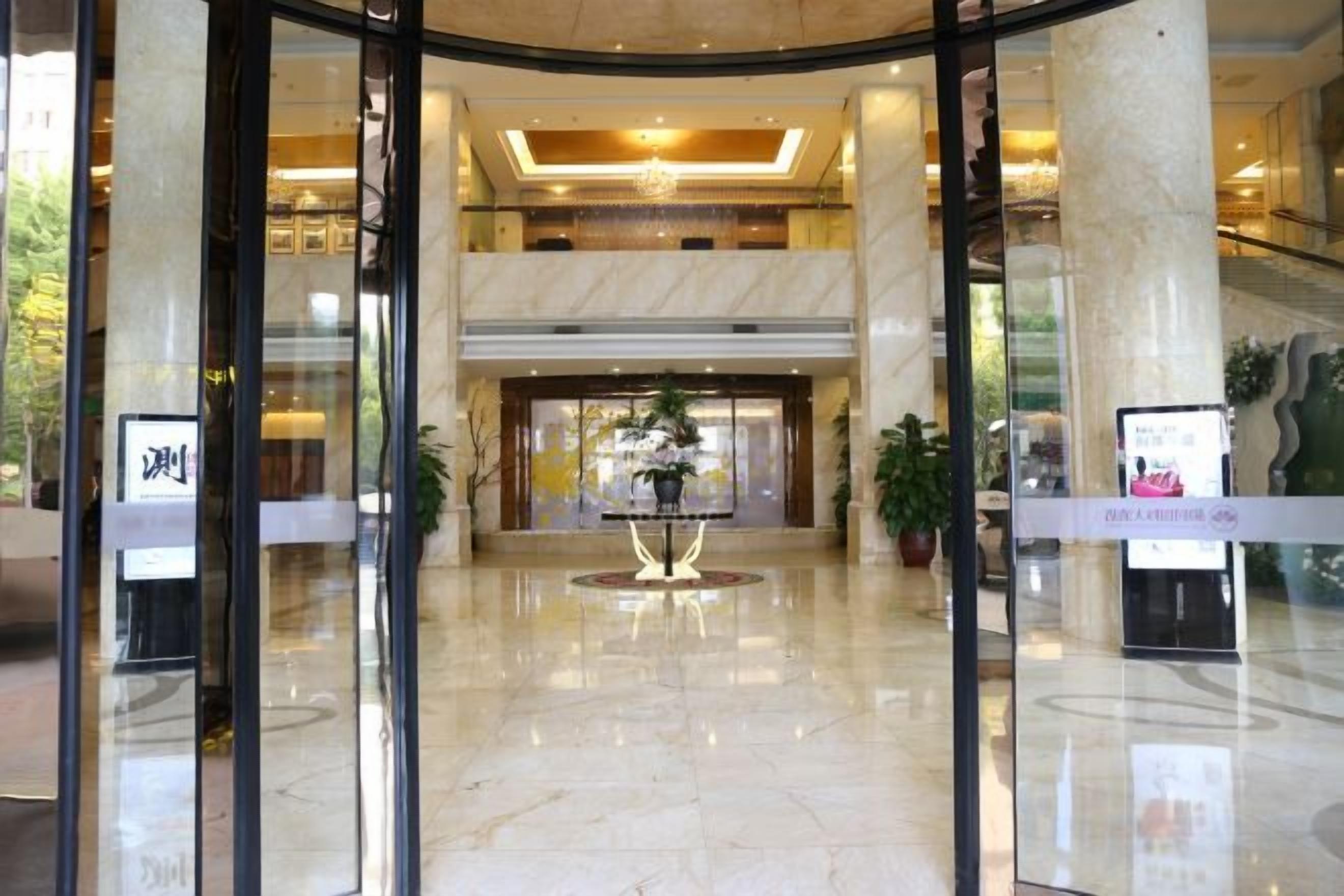 A hotel lobby with a marble floor, glass doors, a reception desk, and a central plant.