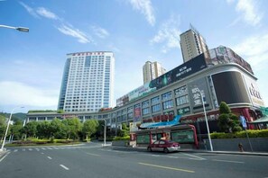 A hotel with a modern facade, a large entrance, and a red bus in front. - Plum Garden International Hotel (Sanming)