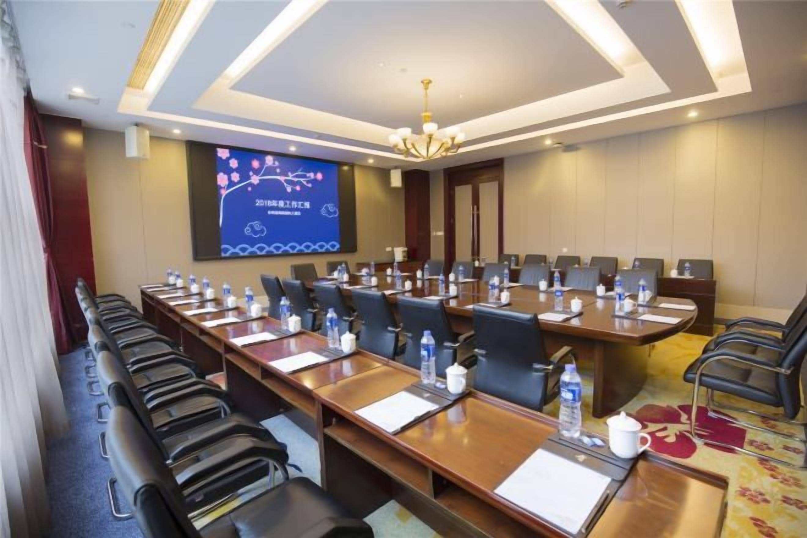Une salle de conférence équipée de longues tables, de chaises et d’un grand écran pour les présentations.