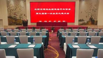 Un salón de conferencias con filas de mesas y sillas, una pantalla grande al frente y una alfombra roja.