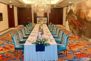 A long conference table with chairs, a chandelier, and a colorful carpet.
