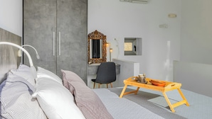 A modern hotel room with a bed, a desk, a chair, and a small table with a bowl and cup.