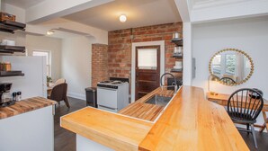 A modern kitchen with a brick wall, wooden countertops, and a central island. - Modern Loft in Historic Birdtown - Unit 4 (Lakewood)