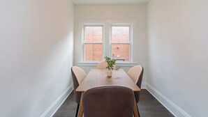 A small, well-lit room with a wooden table and four chairs, a potted plant, and two windows with a brick wall view. - Modern Loft in Historic Birdtown - Unit 4 (Lakewood)