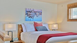 Een netjes ingerichte slaapkamer met een bed, twee nachtkastjes, een rode plaid en een schilderij van een haven op de muur.