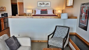 Een compacte hotelkamer met een bed, een stoel, een tafeltje en een bank. Er is een kitchenette met een magnetron en een koelkast.