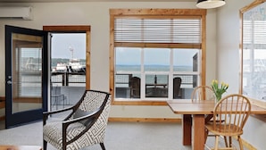 Een kamer met een groot raam met uitzicht op een haven, een eettafel met stoelen, en een gestreept fauteuil.